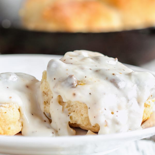 Close-up of fluffy biscuits covered in creamy white gravy with visible black pepper flakes.