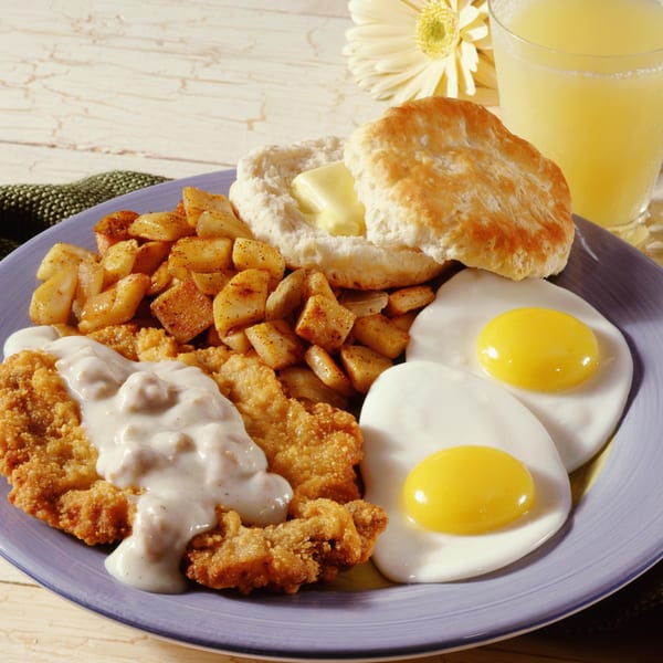 Chicken fried steak with gravy, home fries, biscuits, fried eggs, and orange juice.