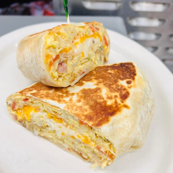 Two halves of a breakfast burrito filled with scrambled eggs, cheese, and ham on a white plate.