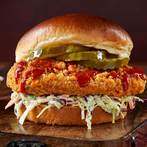 Crispy fried chicken sandwich with coleslaw, pickles, and barbecue sauce on a brioche bun.