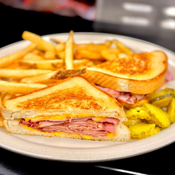 Grilled ham and cheese sandwich with fries and pickles on a white plate at The Fried Egg.