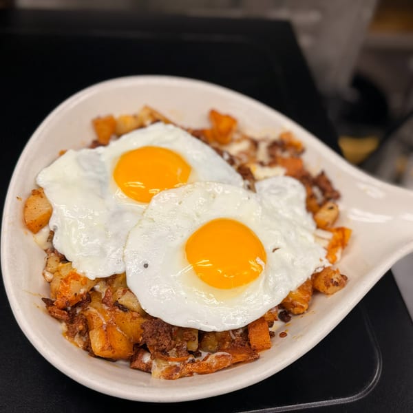 Two perfectly fried eggs with bright yellow yolks atop a bed of crispy breakfast potatoes and chorizo.