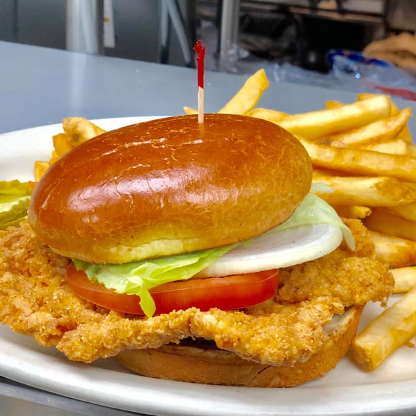 A crispy chicken sandwich with lettuce, tomato, and onion, served with a side of french fries.