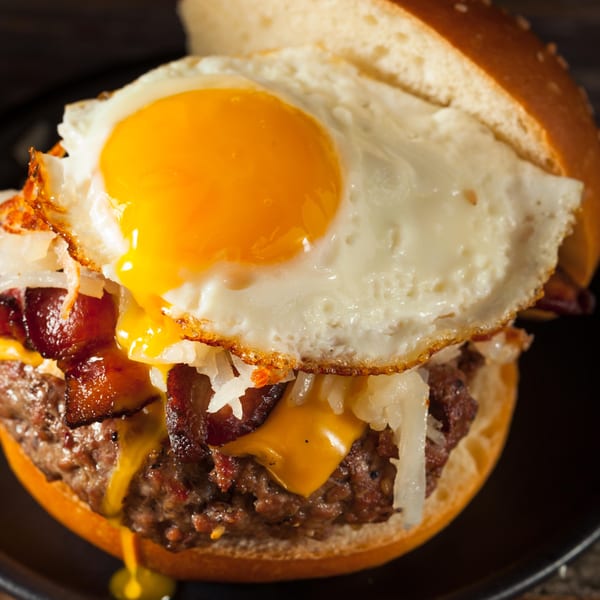 A close-up of a breakfast burger with a fried egg, bacon, cheese, and hash browns.
