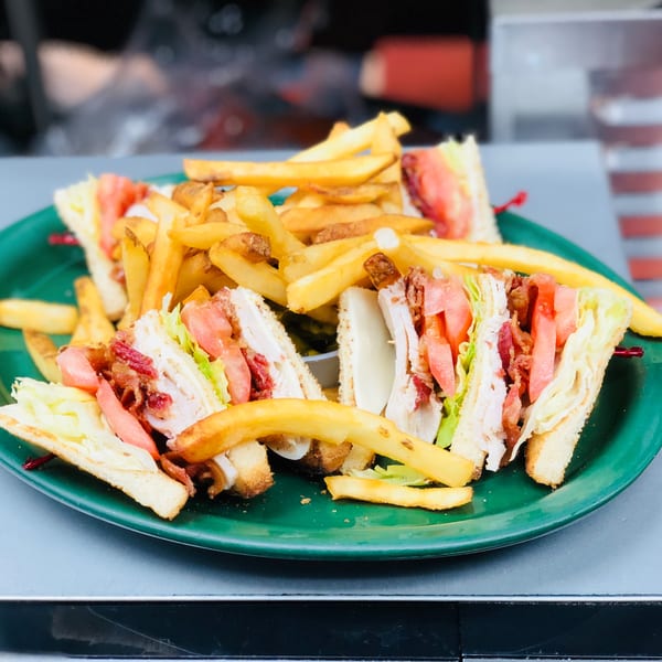 Club sandwiches with bacon, lettuce, tomato, and turkey, served with a side of french fries.