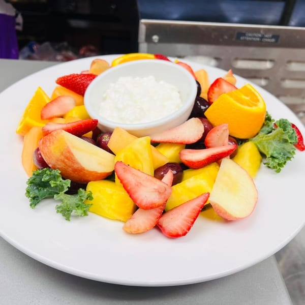 A colorful fruit salad with cottage cheese, oranges, strawberries, apples, and kale on a white plate.